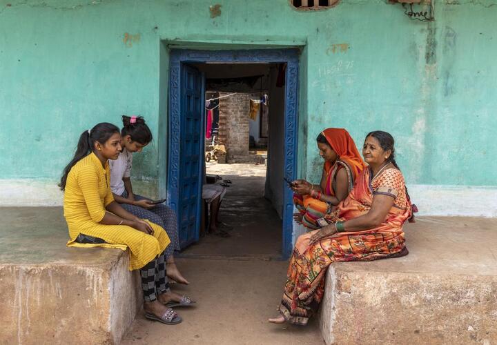 Four women sitting in front of a doorway. Two are using smartphones.