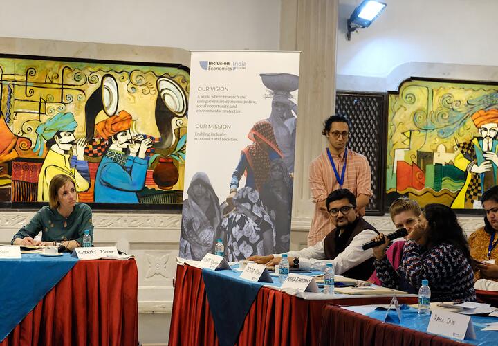 People sitting at various tables, with a woman holding a mic, asking a question. 